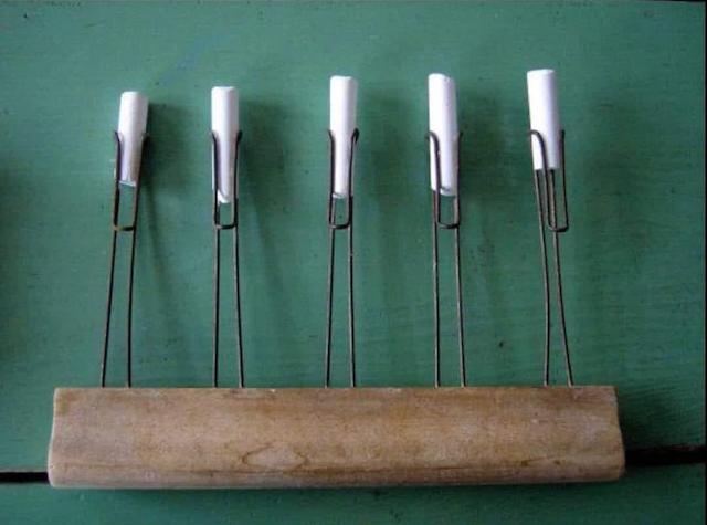 A wooden handle with metal clips, holding pieces of chalk. This vintage tool was used to create multiple lines on a chalkboard simultaneously.